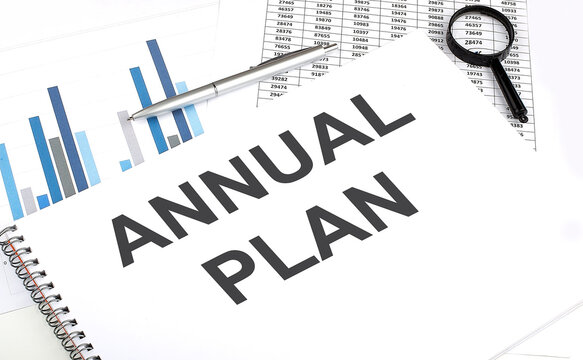 In the notebook, the text ANNUAL PLAN , next to magnifier and a pen, the background is graphics.