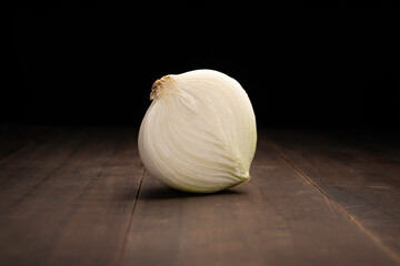 image of a half an onion close up on rustic wooden surface and black background