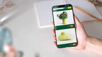 Poster - Close up woman hand holding grocery online store mobile apps on table sitting at home top view,online order concept