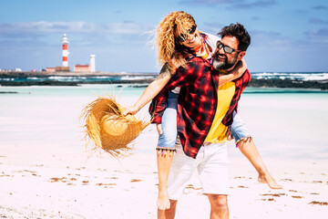 Happy people couple enjoy relationship and summer holiday vacation together laughing and having fun - man carry woman and enjoy the beach outdoor leisure activity with love and friendship