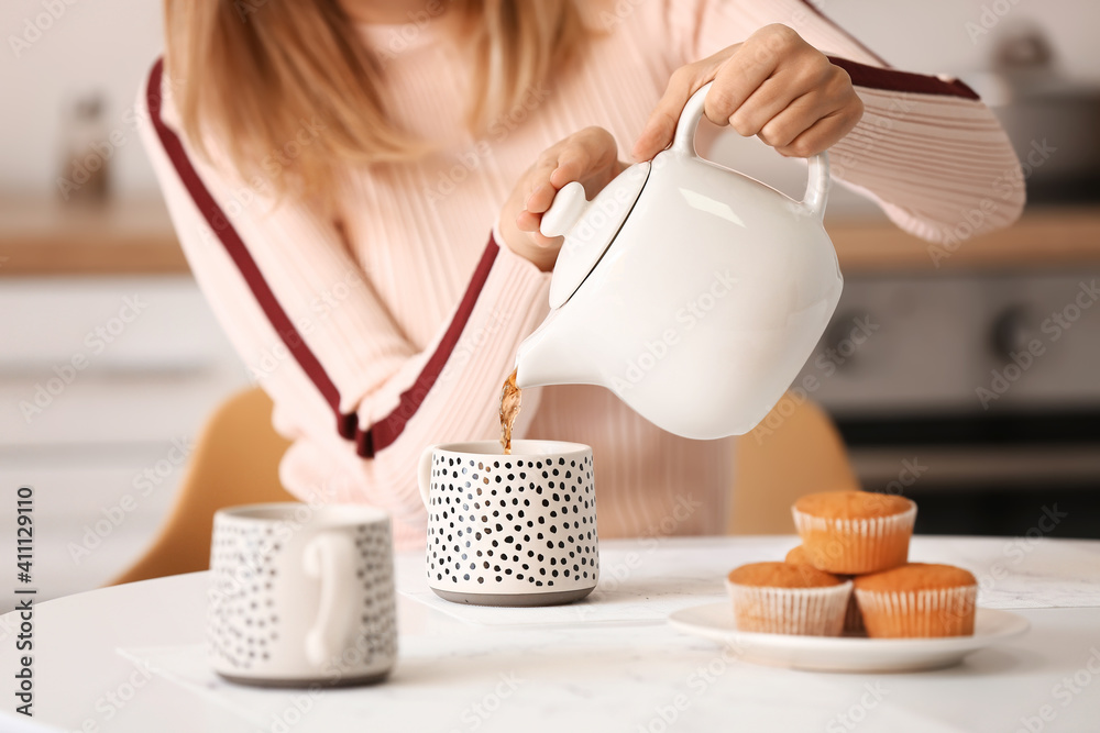 Woman pouring hot tea from teapot into cup at table