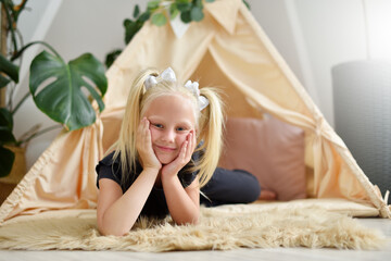 little girl with a smile in her room on the floor next to the wigwam tent