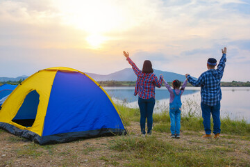 Wall Mural - Back view of asian family watching sunset in the evening at camping site by the lake. Family activity adventure on vacation.