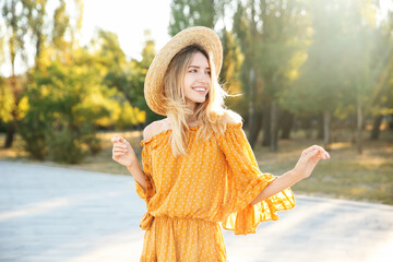 Beautiful young woman in stylish yellow dress and straw hat outdoors