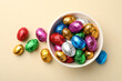 Chocolate eggs wrapped in colorful foil on beige background, flat lay