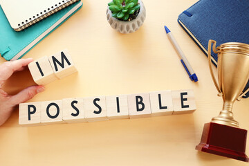 Poster - man hand holding wooden cubes with the text impossible, removing the word im so it written possible. success and challenge concept.