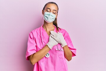 Wall Mural - Young hispanic woman wearing doctor uniform and medical mask smiling with hands on chest, eyes closed with grateful gesture on face. health concept.