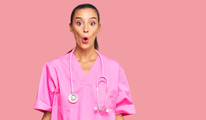 Wall Mural - Young hispanic woman wearing doctor uniform and stethoscope scared and amazed with open mouth for surprise, disbelief face