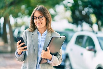 Wall Mural - Young hispanic businesswoman smiling happy using smartphone at the city.