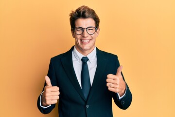 Handsome caucasian man wearing business suit and tie success sign doing positive gesture with hand, thumbs up smiling and happy. cheerful expression and winner gesture.