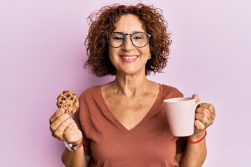 Poster - Beautiful middle age mature woman drinking a cup of coffee and cookie smiling with a happy and cool smile on face. showing teeth.