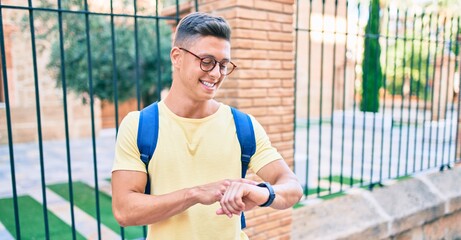 Wall Mural - Young hispanic student smiling happy pointing with finger to the watch at street of city