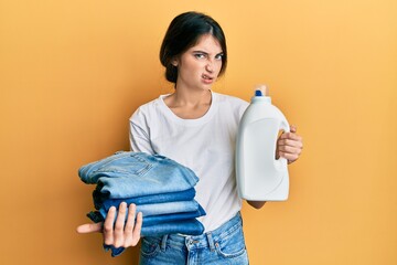 Sticker - Young caucasian woman doing laundry holding detergent bottle and folded jeans skeptic and nervous, frowning upset because of problem. negative person.