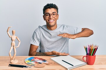 Canvas Print - Young handsome african american man painter sitting palette and art manikin gesturing with hands showing big and large size sign, measure symbol. smiling looking at the camera. measuring concept.