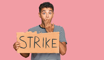 Sticker - Young handsome african american man holding strike banner cardboard covering mouth with hand, shocked and afraid for mistake. surprised expression