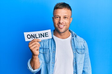 Sticker - Handsome muscle man holding online word on paper looking positive and happy standing and smiling with a confident smile showing teeth