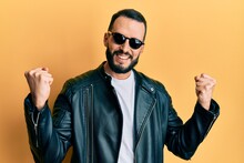 Young Man With Beard Wearing Black Leather Jacket And Sunglasses Screaming Proud, Celebrating Victory And Success Very Excited With Raised Arms