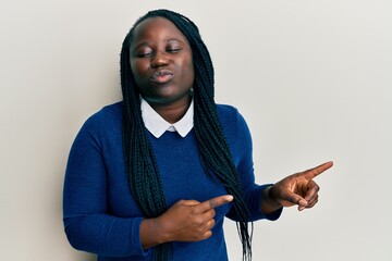 Poster - Young black woman with braids pointing up with fingers to the side looking at the camera blowing a kiss being lovely and sexy. love expression.