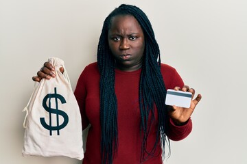 Poster - Young black woman with braids holding dollars bag and credit card skeptic and nervous, frowning upset because of problem. negative person.