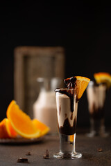 Wall Mural - Sweet cocktail in shot glass with chocolate,cream liqueur,fresh oranges on dark background.Close up.Bar menu,recipes.