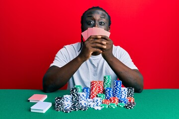 Sticker - Handsome young black man playing gambling poker covering face with cards puffing cheeks with funny face. mouth inflated with air, catching air.