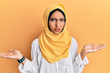 Poster - Young brunette arab woman wearing traditional islamic hijab scarf clueless and confused with open arms, no idea concept.