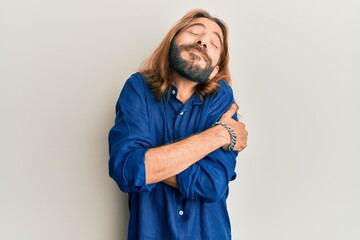 Attractive man with long hair and beard wearing casual clothes hugging oneself happy and positive, smiling confident. self love and self care