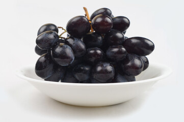 Closeup of fresh shiny black grapes on a white plate