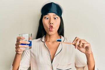 Sticker - Young chinese woman wearing pajama using toothbrush and mouthwash making fish face with mouth and squinting eyes, crazy and comical.