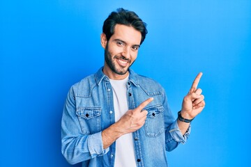 Sticker - Young hispanic man wearing casual clothes smiling and looking at the camera pointing with two hands and fingers to the side.