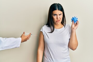 Sticker - Beautiful brunette woman getting vaccine holding coronavirus toy clueless and confused expression. doubt concept.