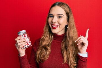 Poster - Young blonde woman holding jar of pills surprised with an idea or question pointing finger with happy face, number one