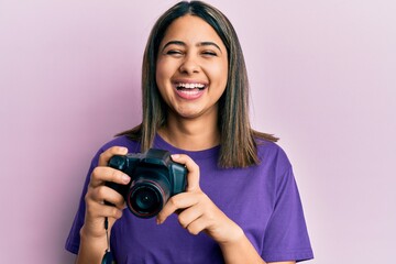 Poster - Young latin woman using reflex camera smiling and laughing hard out loud because funny crazy joke.