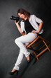 © Михаил Гута - Attractive girl photographer sits on a chair with a camera in her hands in the studio on a gray background.