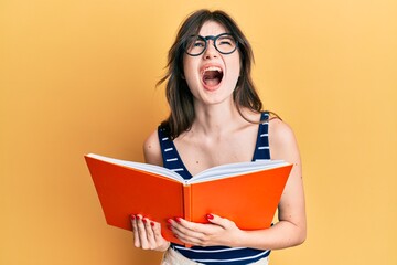 Sticker - Young beautiful caucasian girl reading a book wearing glasses angry and mad screaming frustrated and furious, shouting with anger looking up.