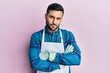 © Krakenimages.com - Young hispanic man wearing apron skeptic and nervous, disapproving expression on face with crossed arms. negative person.