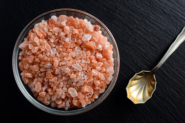 Glass bowl of himalayan salt and small spoon on black background