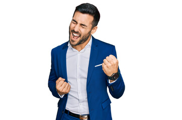 young hispanic man wearing business jacket celebrating surprised and amazed for success with arms ra