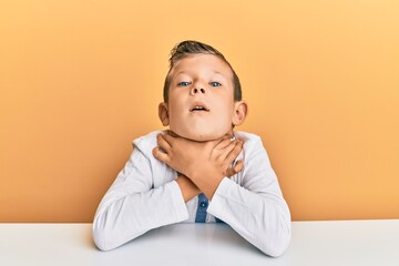 Adorable caucasian kid wearing casual clothes sitting on the table shouting and suffocate because painful strangle. health problem. asphyxiate and suicide concept.