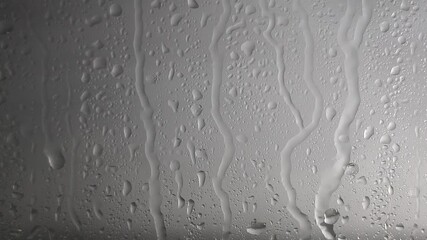 Wall Mural - Raindrops of water flow down the glass in rainy weather on a grey blurred background. Texture and effect of rain on the window