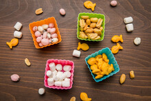 Silicone Cups On Wooden Table Holding Snacks Of Peanuts, Marshmallows, Fish Cheese Crackers, And Yogurt Covered Raisins - Snacks Scattered Around