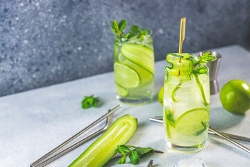 Detox cocktail with mint, cucumber and lime or mojito cocktail in highball glasses on a gray concrete stone surface background.