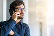 © Joao - Casual man wearing glasses talking on the phone. Successful male portrait at the office by the window