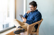 © Joao - Casual business man wearing glasses sitting looking at his tablet. Successful male portrait with thinking face expression working from home by the window