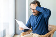 Casual man looking surprised reading bills to pay. Taxes, bank statement and loan debt. Male portrait with worried face and hand on his head