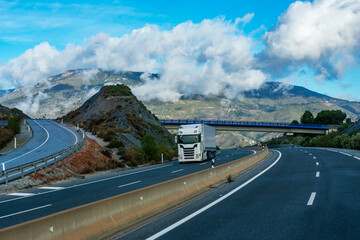 Wall Mural - Truck with refrigerated semi-trailer driving on the highway and with a landscape of mountains and clouds in the background.