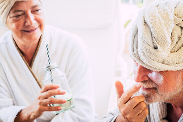 couple of two seniors or mature people taking a drink or cocktail together at home or in a hotel in a massage treatment