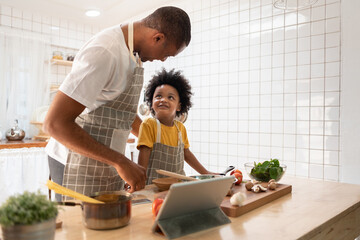 Wall Mural - Black African American Father and son doing online cooking with digital tablet in kitchen