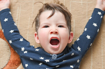 Portrait of boy yawning while lying on the floor. Cute caucasian toddler boy in the pajamas. Waking up concept.