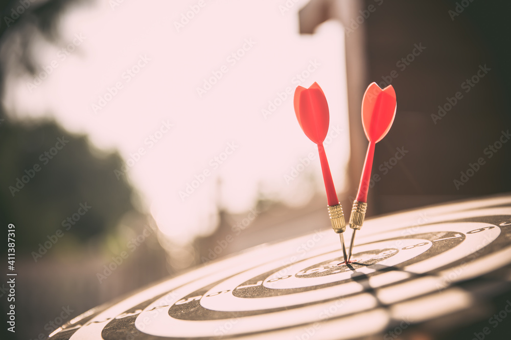 Close-up the bullseye target or dart board has red dart arrow throw hitting the center of a shooting with the sun shines and shadows for business targeting and winning goals business concepts - obrazy, fototapety, plakaty 